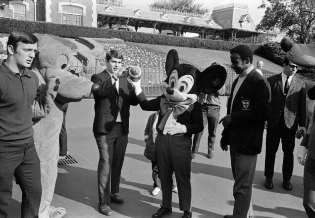 Boston University football players show Mickey Mouse how to properly hold and throw a football at Disneyland on December 7, 1969.