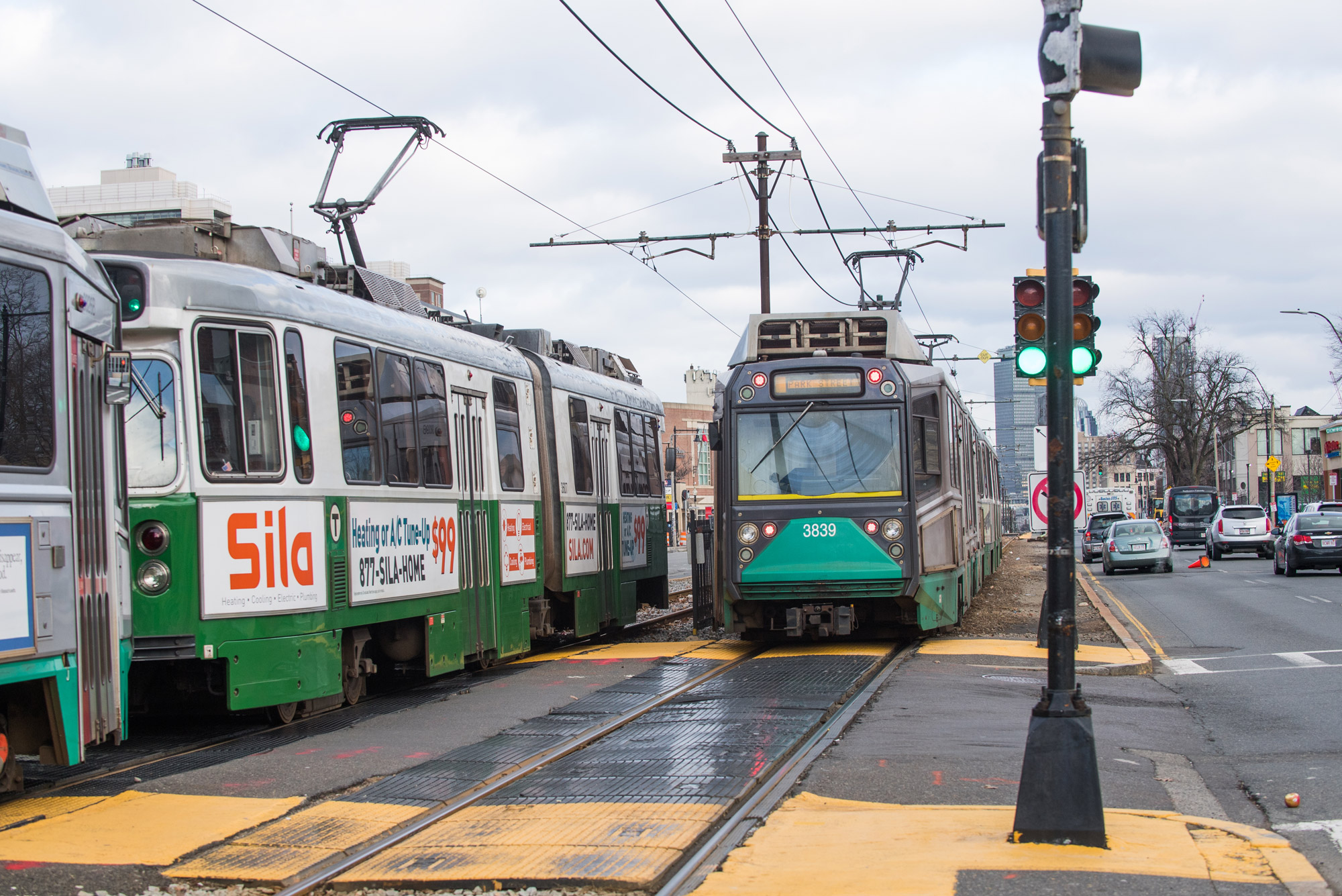 Two greenline MBTA trains pass along Commonwealth Avenue.
