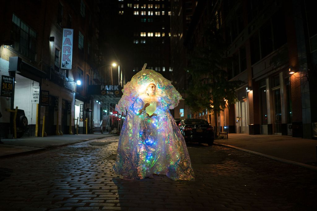 An artist shows off their work during the Boston Illuminus festival. They are draped in bright sparkly fabric. 