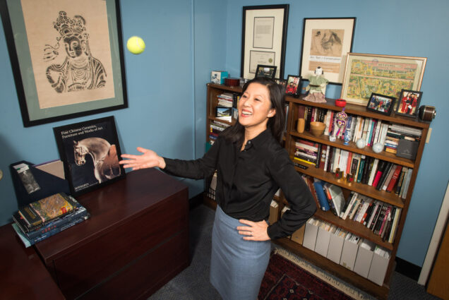 A photo of Alice Tseng standing in her office throwing a tennis ball up in the air.