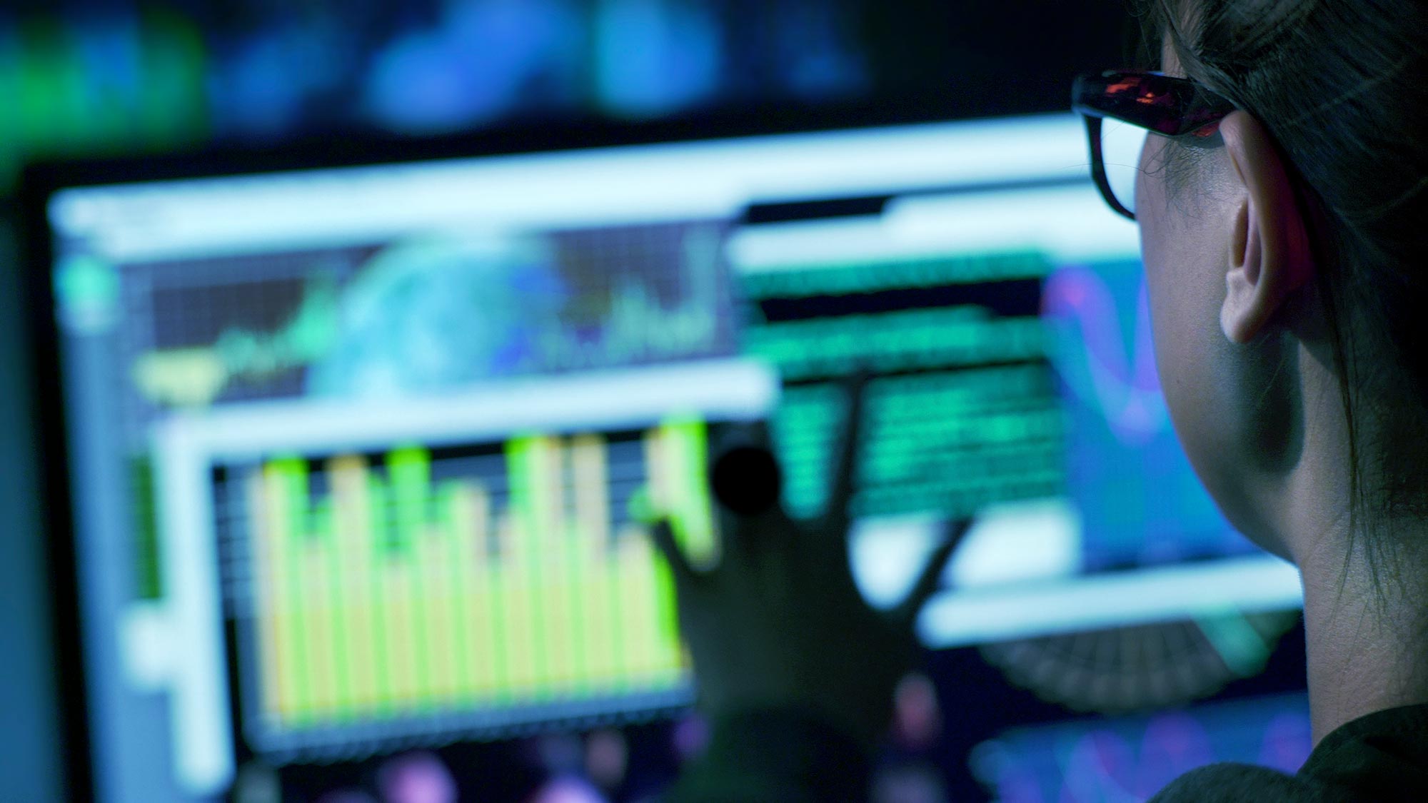 View over the shoulder of a woman working with data on a computer screen.