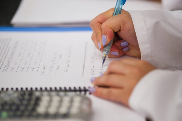 Image of a person holding a pen taking a test; a calculator is at their left.