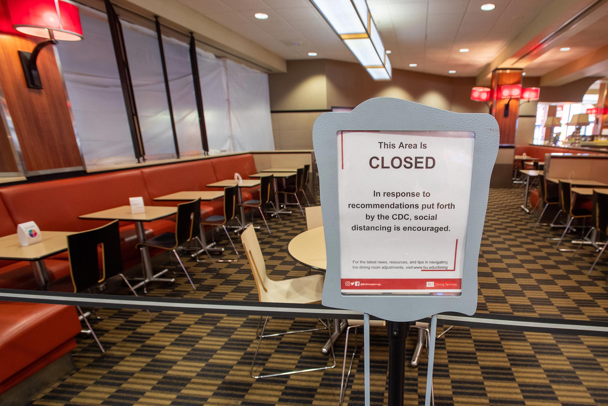 Photo of a sign that says: "This Area is CLOSED in response to recommendations put forth by the CDC, social distancing is encouraged. For the latest news, resources, and tips in navigating the dining room adjustments, visit www.bu.edu/dining" The George Sherman Union dining area and other eateries closed to on-premises patrons this week as a precaution against COVID-19.