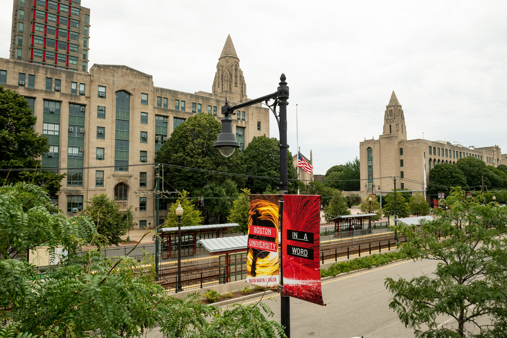 A photo of the Charles River Campus at the beginning of summer; a "Boston University, in a word" banner hangs in the foreground.
