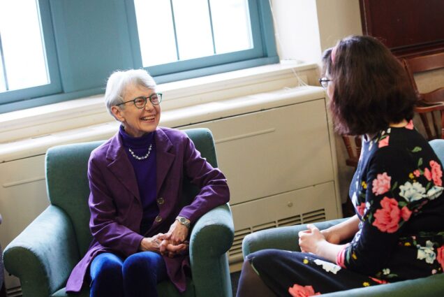 Photo of Dean Mary Elizabeth Moore, in a purple sweater, sitting and chatting with Elizabeth Hurd (STH’19).