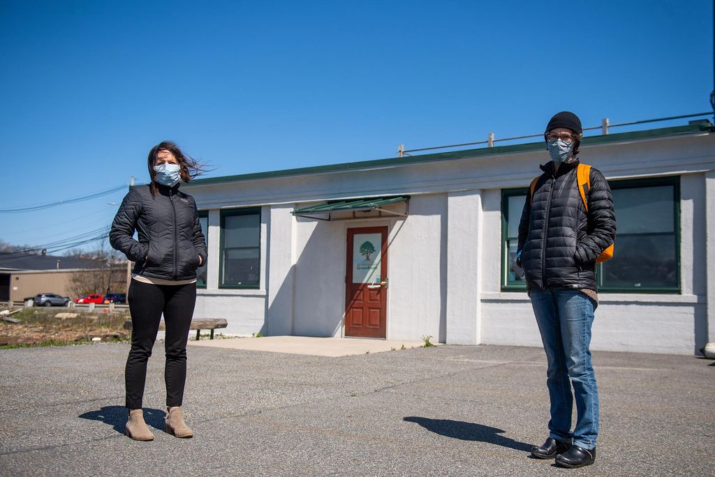 Image of Roseann Bongiovanni (CAS '99, SPH '01), Executive Director at GreenRoots, left, and Madeleine Scammell, Ph.D, professor at SPH and Chair at GreenRoots on April 23, 2020 outside the GreenRoots office. A blue sky is seen in the background. Both women wear masks.