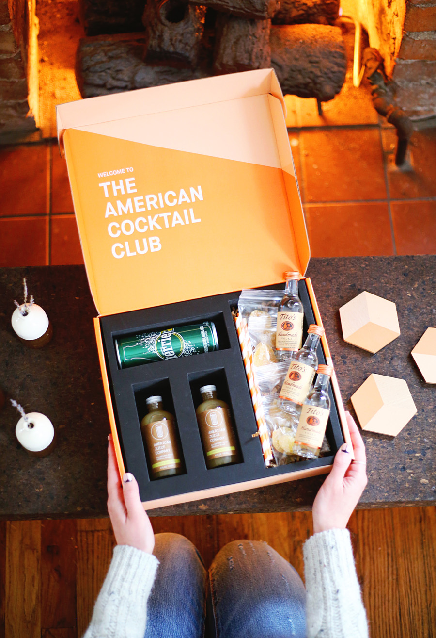 Two hands grab an orange box that reads "The American Cocktail Club" contains mini Tito's vodka bottles and mixers.