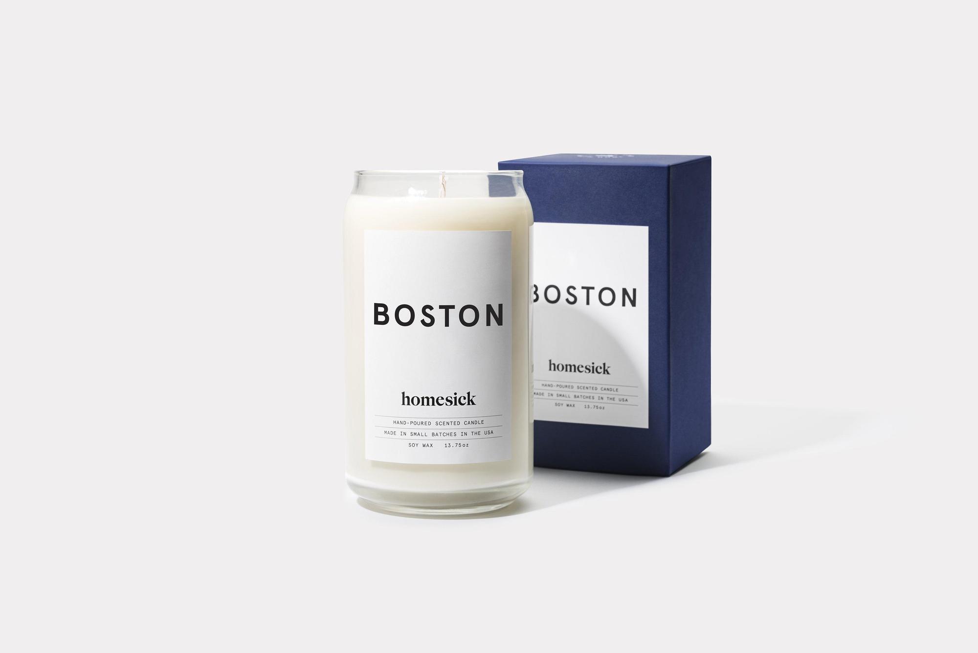 Image a Homesick Boston Candle inside a glass with white wax. A blue box that says 'Boston' on it sits behind it.