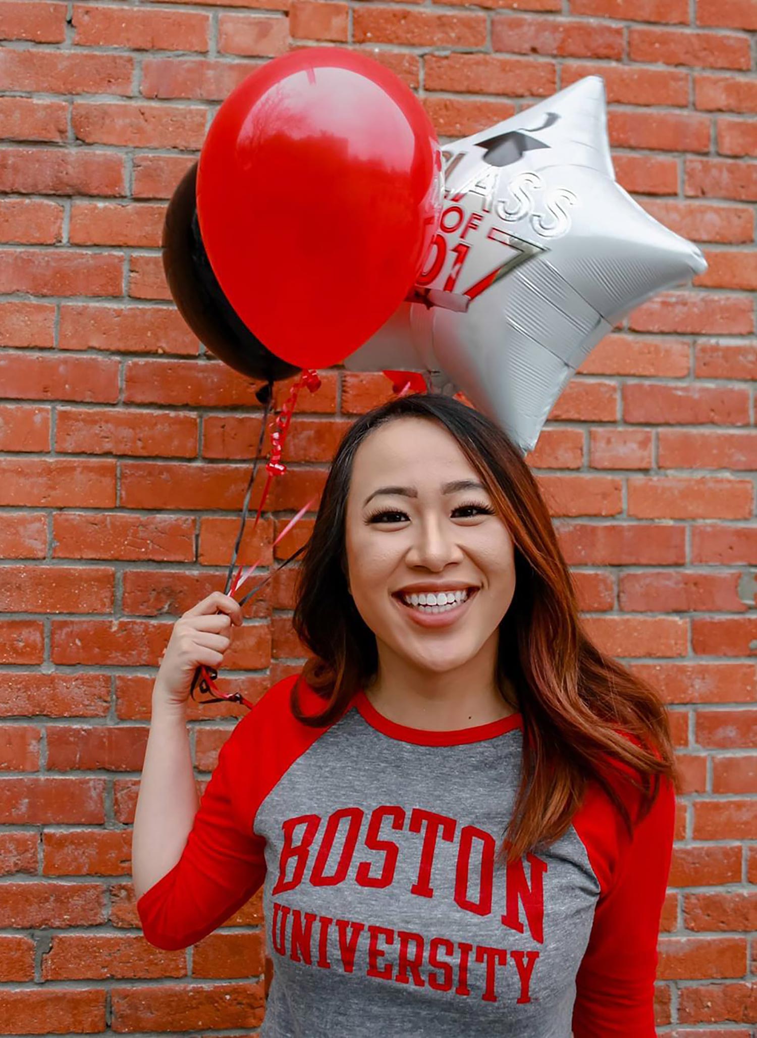 A photo of Geneve Lau holding scarlet and white balloons and wearing a Boston University shirt