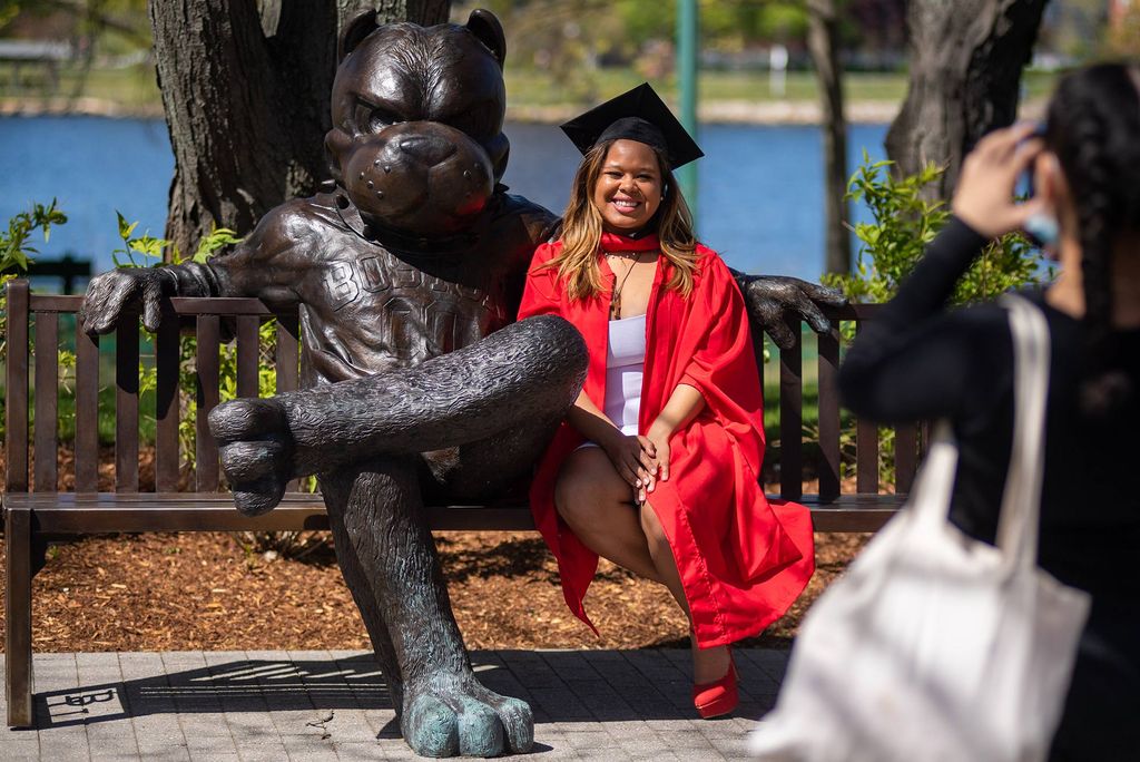 Jessica Diaz (Pardee’20) poses with Rhett at the Rhett bench near the Alan and Sherry Leventhal Center May 14, 2020. Her cousin, Angie Calero of New York City, is pictured in the foreground. Diaz wears her cap and gown. 