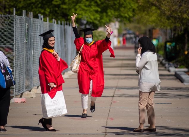 Amna Mira (SAR’20), center, runs to catch up with friends Sara Azhar (SAR’20), at left, and Shahad Benafif (MGH IHP) May 14, 2020 on a sidewalk near BU. Two girls wear red gowns and caps.