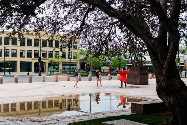 Students came to campus to step on the seal on the day that would've been Boston University Commencement. A tree and puddle are seen in the foreground, a student in cap and gown poses triumphantly over the seal in the background.