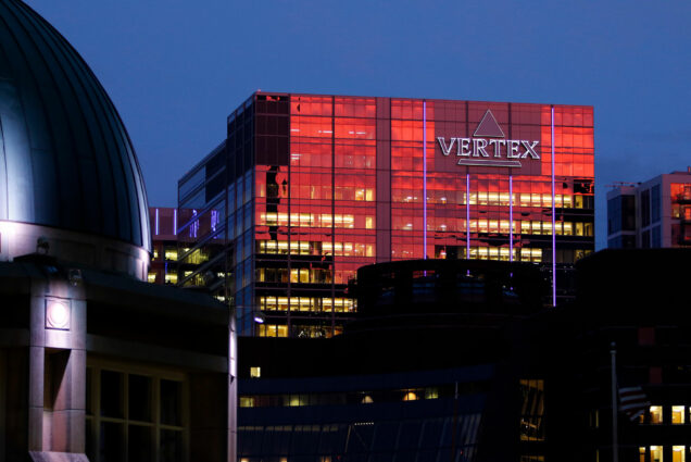 The sunset reflects off the Vertex Pharmaceuticals headquarters building, Thursday, Sept. 21, 2017 in Boston's Seaport. A sign on the building reads 'Vertex' in purple. The top dome of a building is seen in the bottom left foreground.