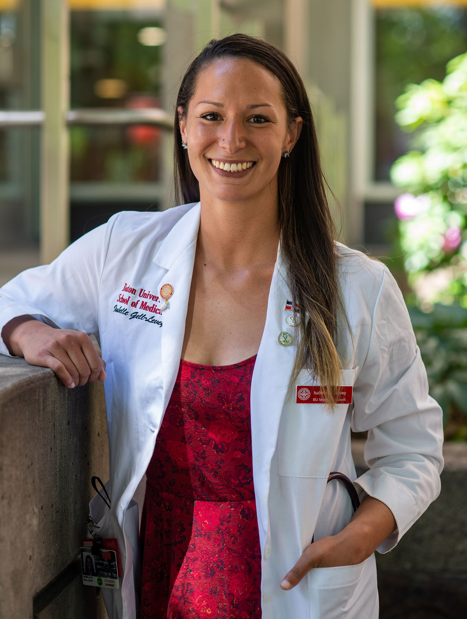 Portrait of Isa Gell-Levey (MED’22) in a white medical coat and a red dress.