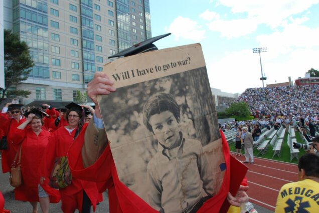 A photo of the Class of 1970 Convocation in 2010. A graduate holds up a newspaper that reads "Will I have to go to war?"