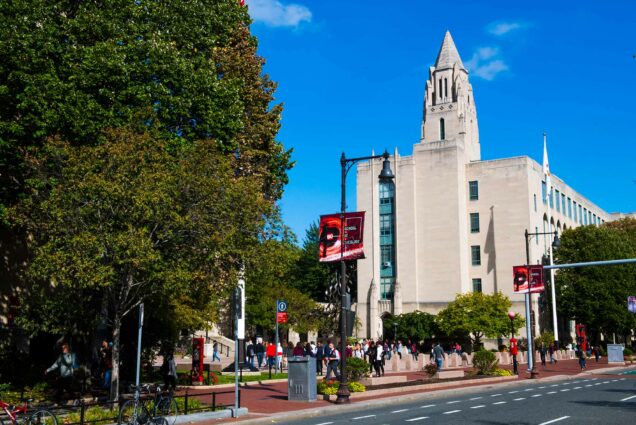Photograph of Marsh Plaza from across the street with CAS building in background. The plaza is busy with people.Red banners seen throughout image. It's a sunny day at the start of the fall semester.
