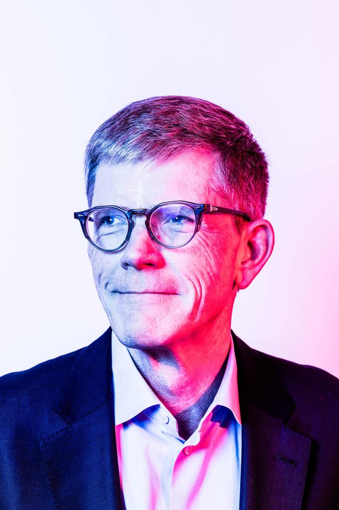 Headshot of Jay Roewe (COM’79) with intense pink and purple light. He smiles and looks off to the side.