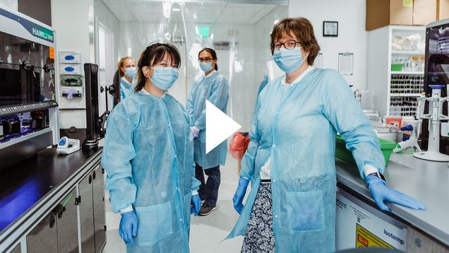 A photo of the team at BU's COVID-19 testing lab. A video play button is overlayed.