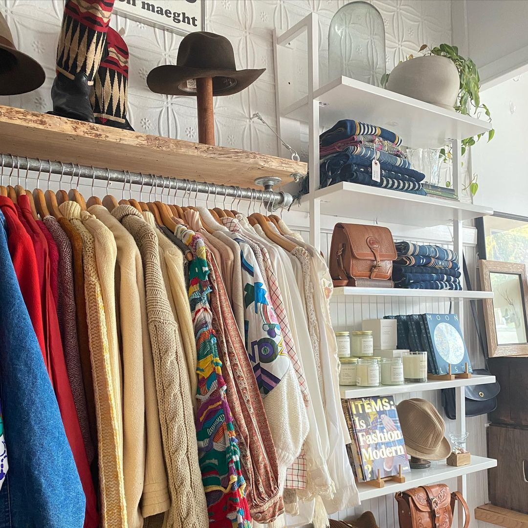 a photo of the interior of We Thieves thrift tores. Clothes, bags, candles, and bags are on display next to a sunny window.