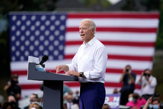 A photograph of Joe Biden giving a campaign speech at a podium with an American flag in the background