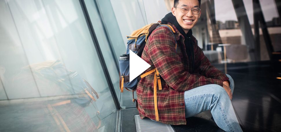 A photo of Joshua Pei smiling at the camera. A white video play button sits over the image.