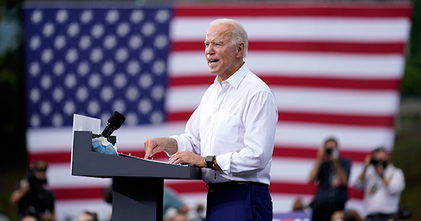 A photograph of Joe Biden giving a campaign speech at a podium with an American flag in the background