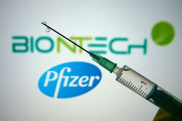 A photo of a needle in front of a sign that reads "Biotech Pfizer"