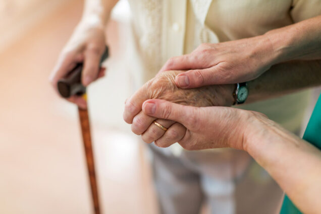 A photo of person holding another person's hand as the use a cane