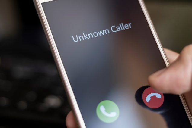 Photo of a cellphone screen that says "Unknown caller" and a thumb pushing the red button to hang up.