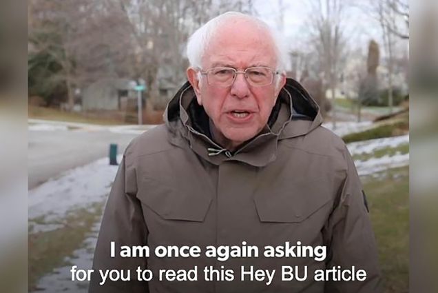 Screenshot of Bernie Sanders in a light brown rain coat from his iconic fundraising campaign video during the 2020 presidential primary. The closed captioning text reads “I am once again asking for you to read this Hey BU article.” Behind, a suburban neighborhood street corner is seen.