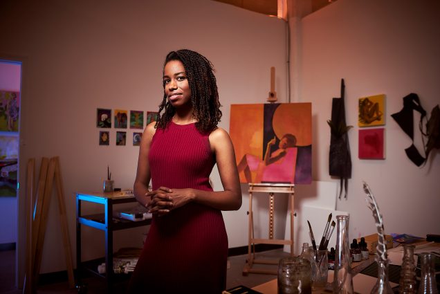 A portrait photo of Adrienne Elise Tarver standing in front of one of her paintings