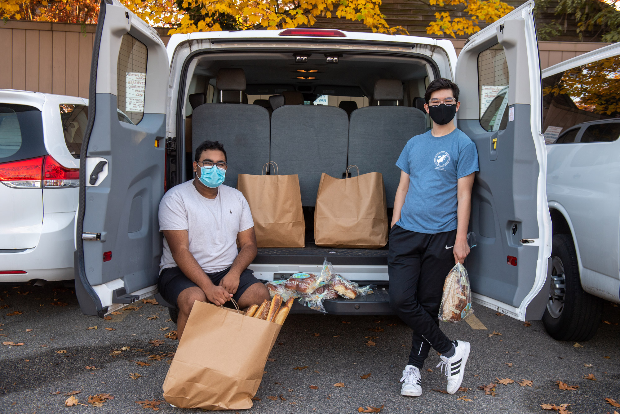 A photo of Saahil Adusumilli (SAR’22), at left, and Michael Gomez (SAR’21) from Student Food Rescue sitting in the back of a van with brown paper bags. They are both wearing masks.