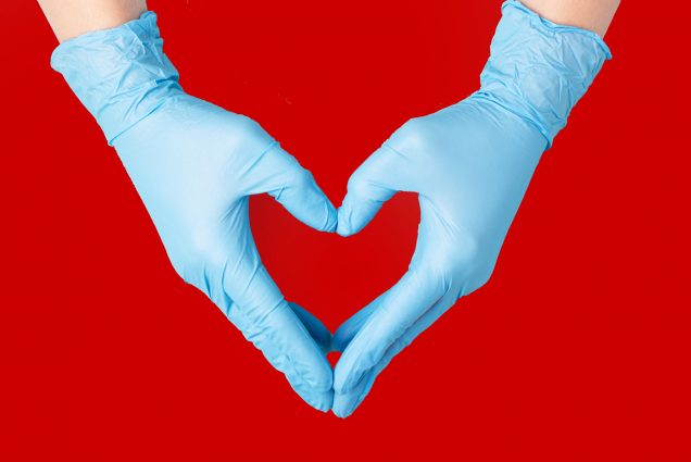 A pair of gloved hands making a heart over a red background