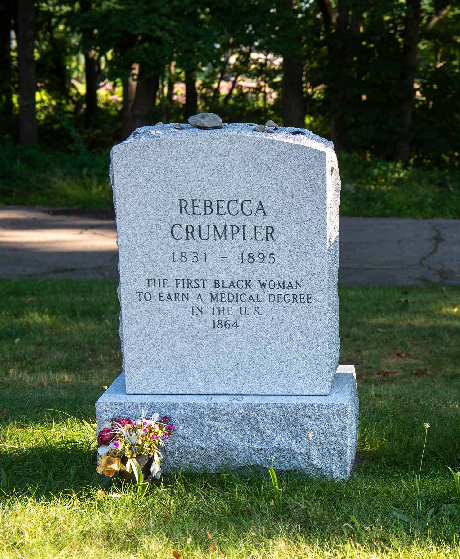 Photo of the headstones of Rebecca Lee Crumpler (MED'1864), and reads “the first Black woman to earn a medical degree in the US, 1831-1895” The headstone is located in the Fairview Cemetery in Hyde Park, and surrounded by lush, green summer grass.