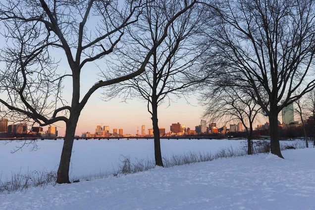 Photo taken on the Boston esplanade near BU looking towards downtown. The river and esplanade are covered in snow; the sky fades to light pink in the distant.