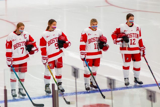 Photo of Senior F Jesse Compher (SHA), Freshman F Clare O'Leary (CAS), Junior F Mackenna Parker (CAS), Junior F Kaleigh Donnelly (CAS) on ice in their hockey uniforms with colorful stripped masks in honor of the Pride Week Celebration put on by BU Athletics.