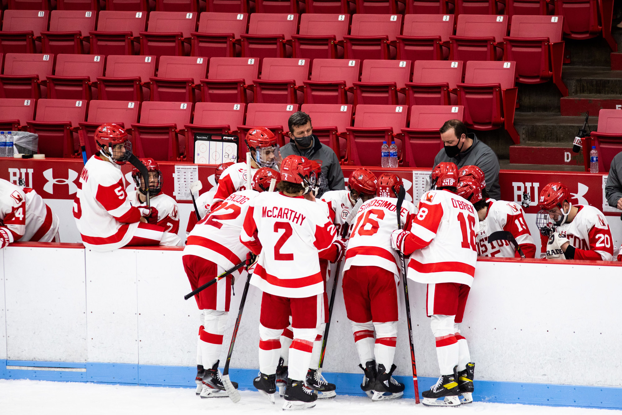 BU Men's ice hockey players huddle around the bench where Coach O'Connell is speaking to them