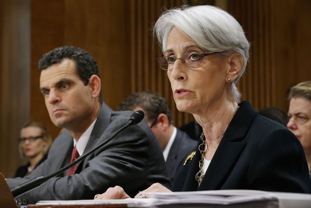 Photo of Wendy Sherman, when she was State Department Undersecretary For Political Affairs, testifying before the Senate Foreign Relations Committee about the ongoing P-5+1 talks with Iran during a hearing in the Dirksen Senate Office Building on Capitol Hill July 29, 2014 in Washington, DC. Sherman has white, ear-length hair and glasses, and speaks into a microphone at a desk with committee members seen blurred in the background.