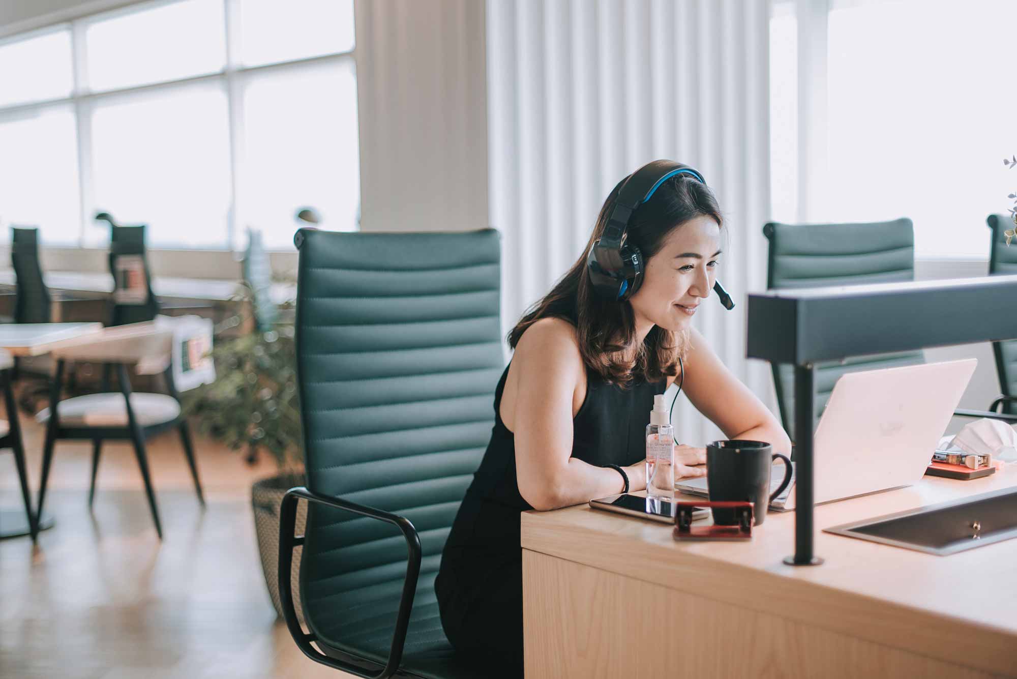 an asian chinese mid-adult white collar worker wearing a headset while participating in a computer video conference