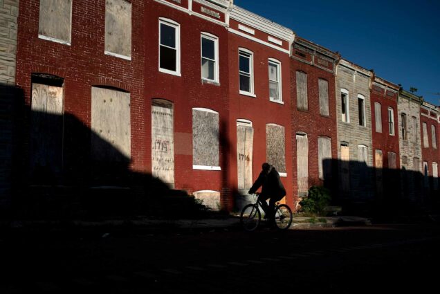 A man rides a bike past boarded up row houses in the Broadway East neighborhood on October 14, 2020, in Baltimore, Maryland.