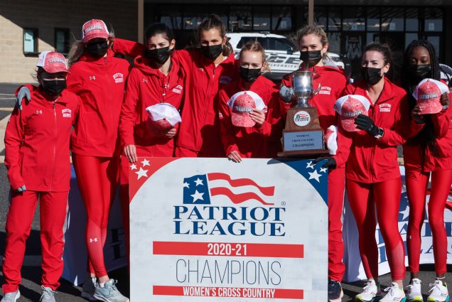 A photo of the women's cross country team standing behind a sign that reads "Patriot League 2020-2021" Champions