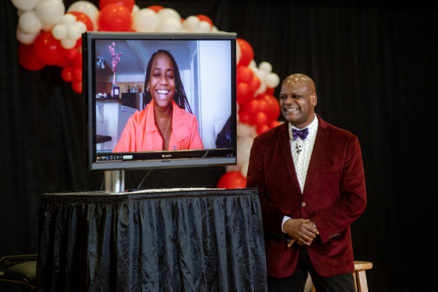 Photo of Dean of students Kenneth Elmore chatting with student commencement speaker Archelle Thelemaque (COM’21), on a video screen, during the class of 2021 senior breakfast broadcast from the GSU April 30. Elmore wears a red velvet blazer and Archelle wears a pink shirt.
