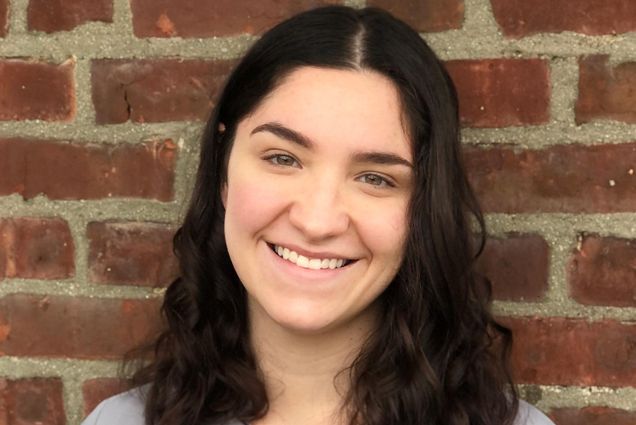 A portrait photo of Alexa Friedman standing against a brick wall