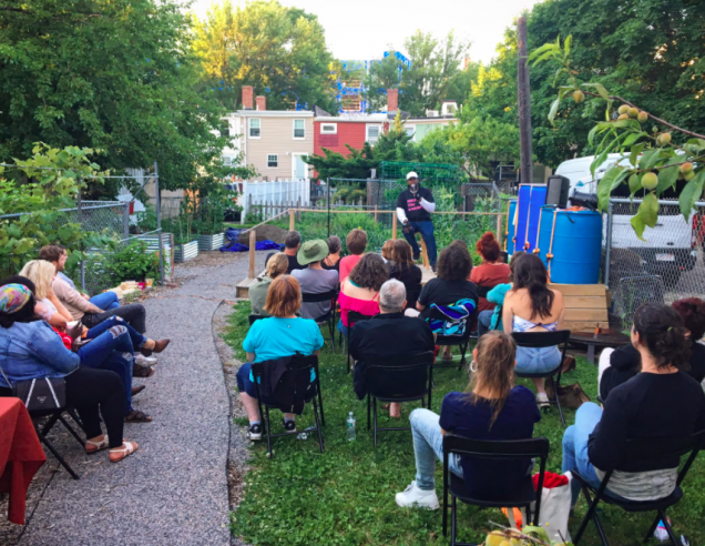 A stand-up comic entertains a small crowd outdoors at Eastie Farms in East Boston, Massachusetts.
