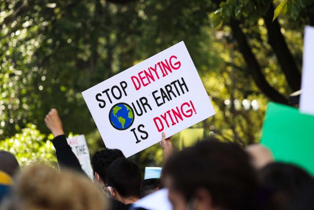 A protester at a Climate Change Action rally holds a sign that says 'Stop Denying Our Earth Is Dying!'