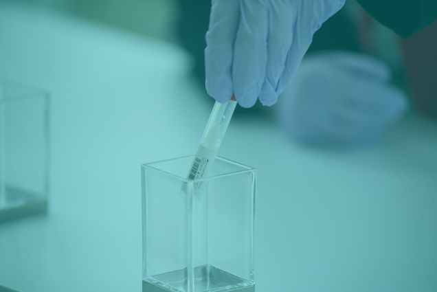 The gloved hand of a medical clinician places a nasal swab used for collecting a COVID-19 test specimen into a container.