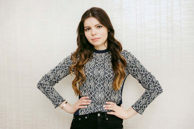 Portrait of Daniella Pierson with her hands on her hips. She has long brown, slightly wavy hair and light skin. She wears a black and white lace blouse and smiles slightly.