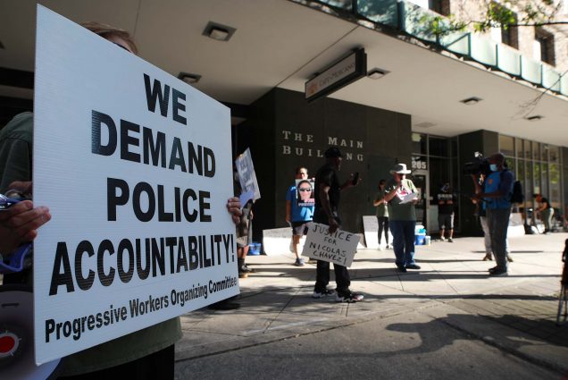 A protestor stands in front of the Houston Police Department headquarters holding a sign that says 'We Demand Police Accountability! Progressive Workers Organizing Committee.'
