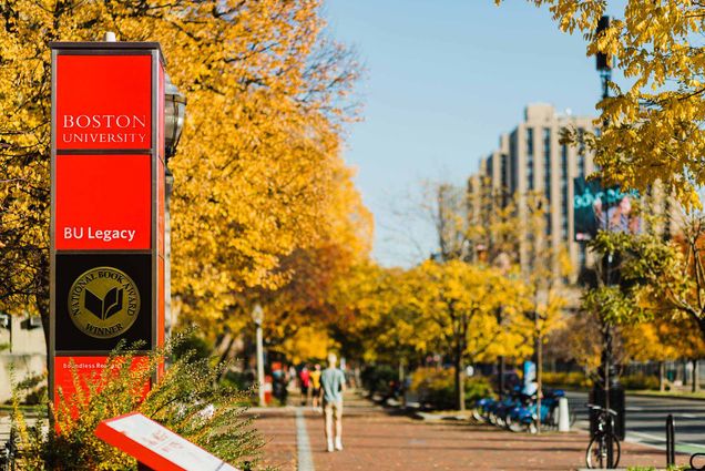 a photo of BU's East campus in the Fall. Yellow leaves border the sidewalks as students walk down the street