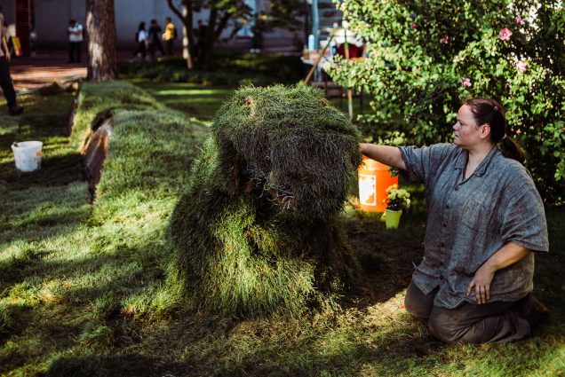 a photo of Sculptor Erin Genia works on her depiction of Unktehi, a water spirit from Native American culture, rising out of the lawn by the School of Theology